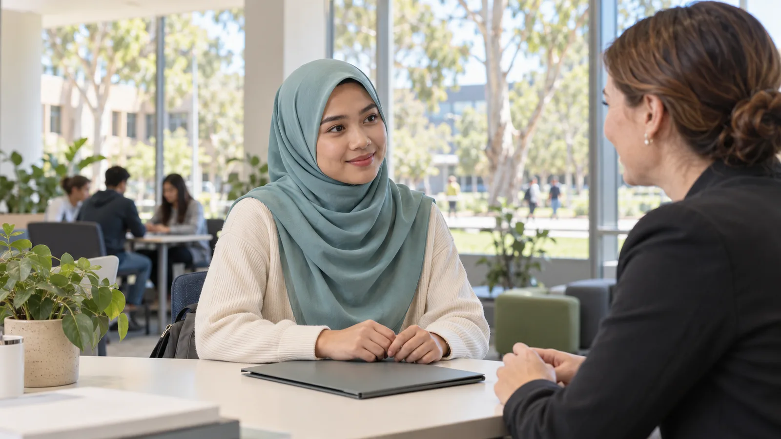 A Malaysian student in a teal hijab speaks with an adviser at a sunlit Australian university.