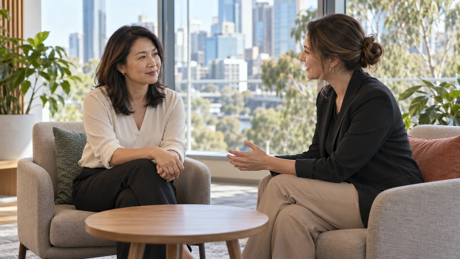 A Malaysian office worker speaks with an employment adviser in a sunlit Australian office about workplace changes.